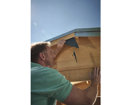 Muž montuje dřevěný dům s úhloměrem.