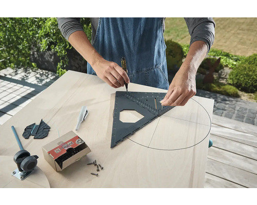 Osoba kreslí kruh na dřevěnou desku pomocí tesařského úhelníku a tužky. Nářadí a šrouby jsou připraveny.