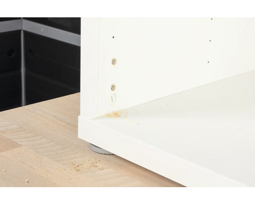 Detail bílého kusu nábytku se šrouby a dřevěnými štěpkami.