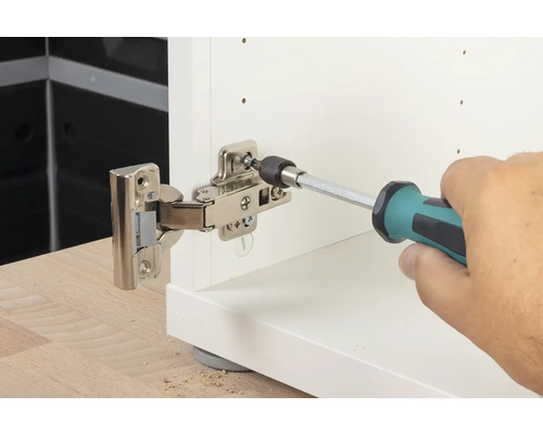 Muž připevňuje pant šroubovákem k bílému kusu nábytku.