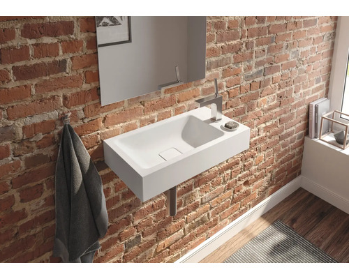 Koupelna s bílým umyvadlem na cihlové zdi, doplněná zrcadlem a armaturami.