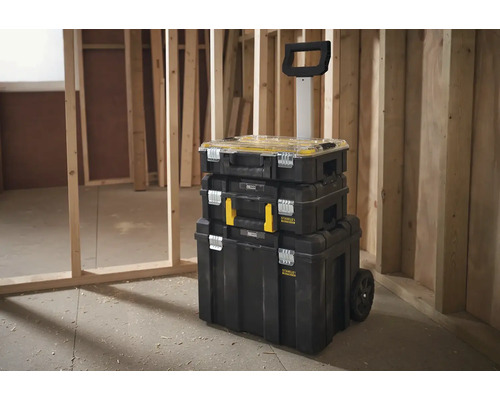 Věž kufříků na nářadí Stanley s rukojetí a kolečky před dřevěnou stěnou