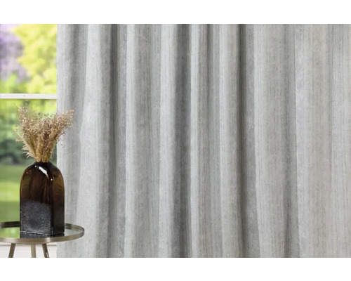 Dekorativní šedý závěs vedle hnědé vázy na kulatém stole