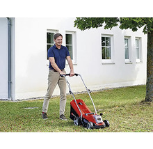 Muž seče trávník červenou sekačkou na zahradě.