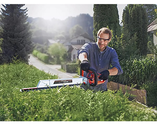 Muž stříhá živý plot nůžkami na živý plot venku.