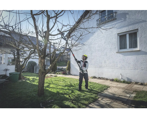 Osoba s ochrannou přilbou používá prořezávač stromů k prořezávání stromu na zahradě.