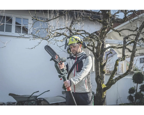 Muž zahradničí s akumulátorovou tyčovou pilou