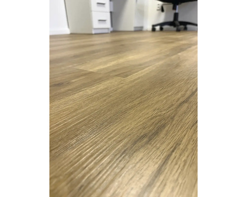 Detail světlé laminátové podlahy s dřevěnou strukturou v místnosti.