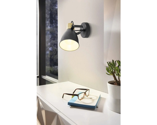 Černé kovové nástěnné svítidlo s dřevěným detailem nad stolem