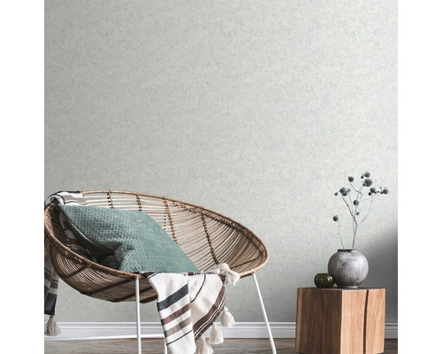 Obývací pokoj s ratanovým křeslem, polštářem, dekou a dřevěným odkládacím stolkem s dekorací před strukturovanou tapetou