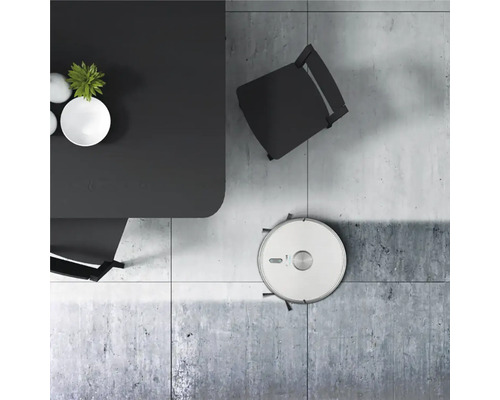 Scéna s robotickým vysavačem pod stolem a židlí na dlažbě