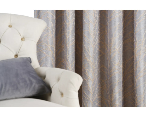 Dekorativní závěs s listovým vzorem vedle křesla.