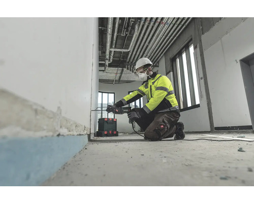 Stavební dělník klečí a vrtá vrtačkou díru do zdi.