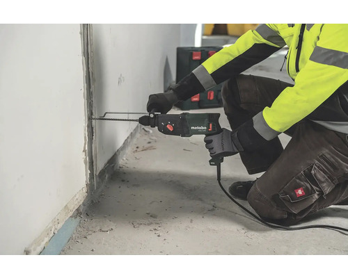 Pracovník vrtá díru do zdi s vrtačkou Metabo.