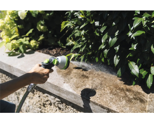 Zahradní scéna s osobou, která používá zahradní sprchu k čištění zdi.