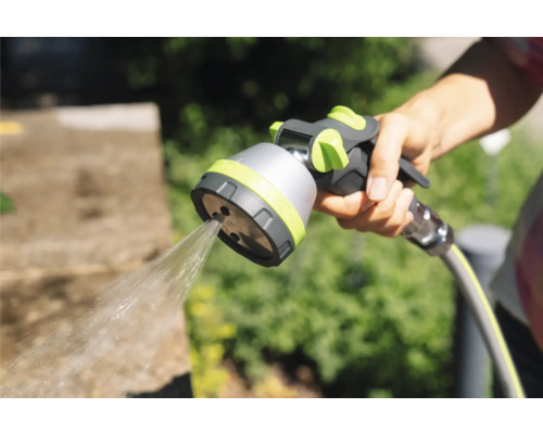 Ruka drží zahradní hadicovou stříkací pistoli s proudem vody.