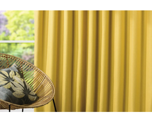 Žlutý závěs vedle ratanového křesla s polštářem.