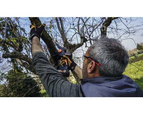 Muž řeže větve stromů akumulátorovou prořezávací pilou.