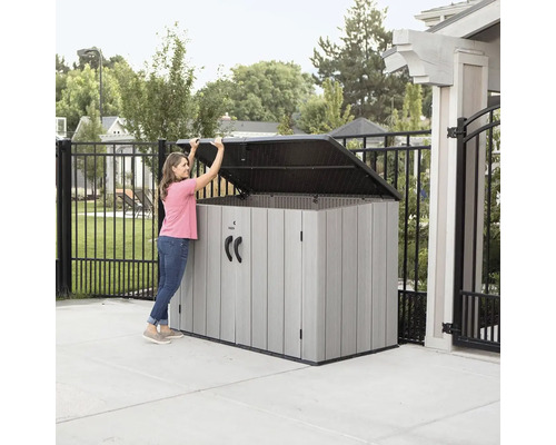 Žena otevírá šedý úložný box venku, který slouží pro skladování.