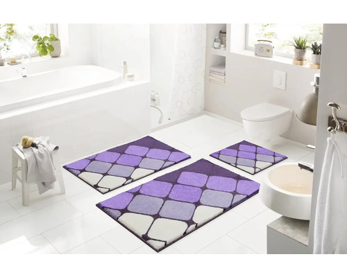 Moderní koupelna s třídílnou, fialovo-šedou sadou koupelnových koberečků s geometrickým vzorem před vanou, umyvadlem a toaletou