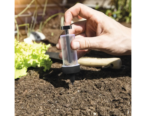 Osoba používá dávkovací pomůcku pro semena v zahradním záhonu