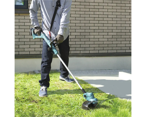 Osoba používá akumulátorový vyžínač na zahradě k sekání trávy.