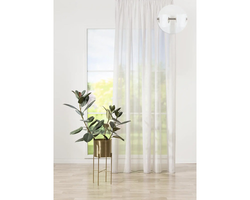 Bílá záclona s očky před oknem, s pokojovou rostlinou v květináči.