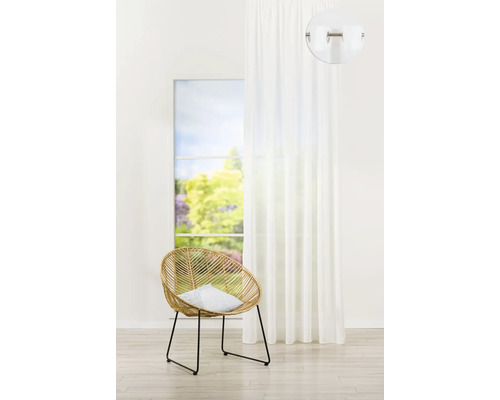 Světlá místnost s ratanovým křeslem, polštářem, bílým závěsem a oknem