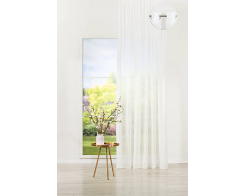 Bílý závěs s očky před oknem s výhledem do zahrady