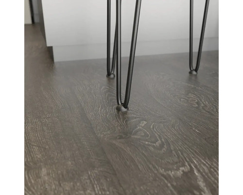 Detail nábytku se třemi černými kovovými nohami na tmavé dřevěné podlaze