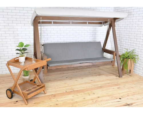 Dřevěná houpačka se světle šedým polštářem a servírovacím vozíkem na terase