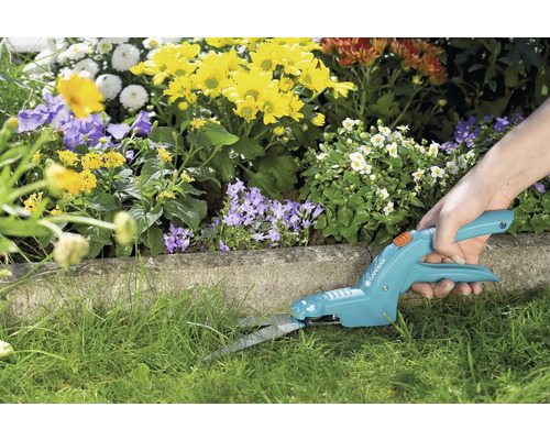 Osoba stříhá okraje trávníku zahradními nůžkami na trávu.