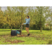 Žena shrabuje podzimní listí do pytle na listí na zahradě