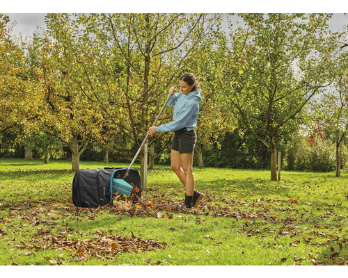 Žena shrabuje podzimní listí do pytle na listí na zahradě