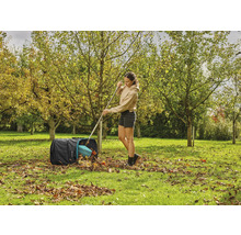 Žena hrabe listí hráběmi do zahradního pytle na zahradě.