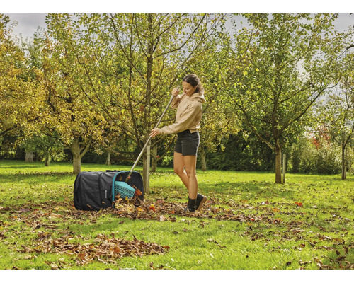 Žena hrabe listí hráběmi do zahradního pytle na zahradě.