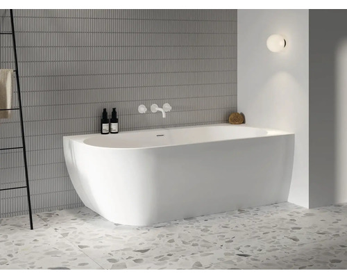 Světlá koupelna s volně stojící vanou, armaturami, držákem na ručníky a nástěnnou lampou