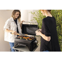Dvě ženy grilují zeleninu a maso na přenosném grilu venku.