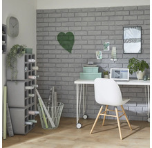 Pracovna se stolem, židlí, policemi a dekorativními předměty před šedou cihlovou zdí