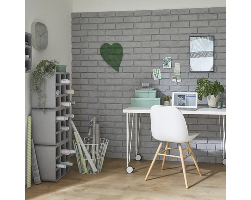 Pracovna se stolem, židlí, policemi a dekorativními předměty před šedou cihlovou zdí