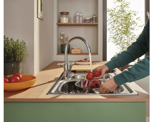 Nerezový dřez s osobou myjící rajčata pod tekoucí vodou