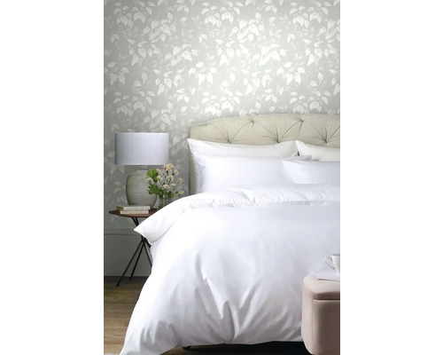 Ložnice s postelí, nočním stolkem a tapetou s listovým vzorem