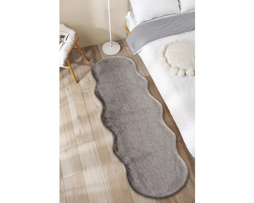Interiérový snímek ložnice s postelí a šedým kobercem ve vzhledu kožešiny.