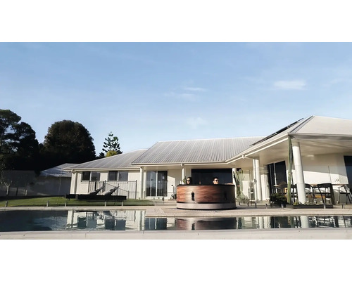 Pohled shora na dřevěnou koupací káď vedle bazénu před obytným domem.