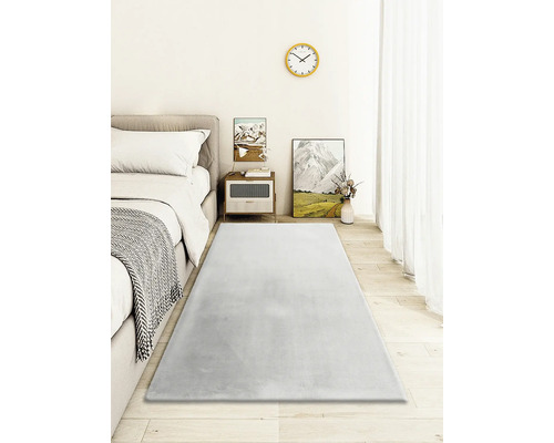 Ložnice s postelí, nočním stolkem a šedým kobercem na dřevěné podlaze.