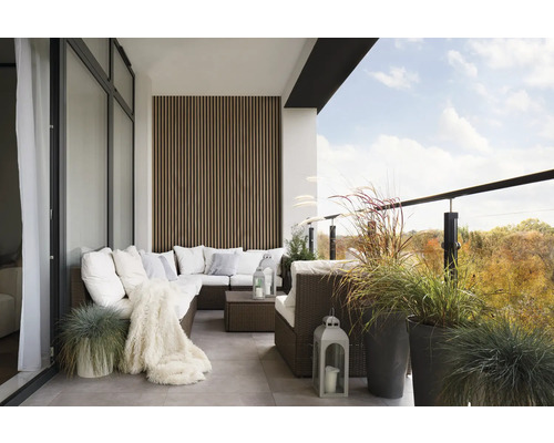 Balkon s ratanovou pohovkou, polštáři, dekou, lucernami a rostlinami v květináčích