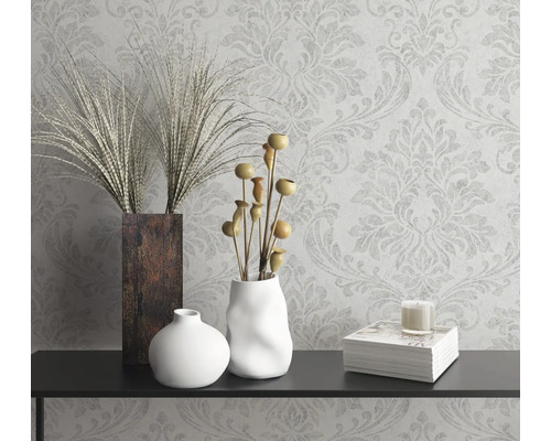 Dekorativní zátiší s vázami, okrasnými rostlinami, svíčkou a knihou na konzole před vzorovanou tapetou