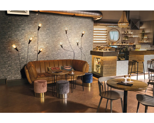 Interiér kavárny s pohovkou, stoly, stoličkami a nástěnnými svítidly před cihlovou zdí