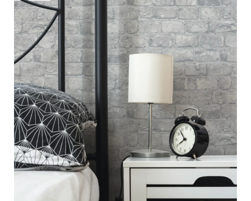 Ložnicová scéna s postelí, nočním stolkem, lampou, budíkem a tapetou se zdiva