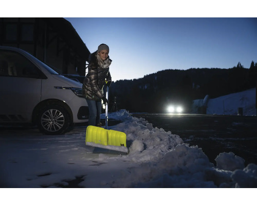 Žena odhazuje sníh lopatou na sníh před autem.